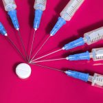 Syringes and pills on a dark pink background